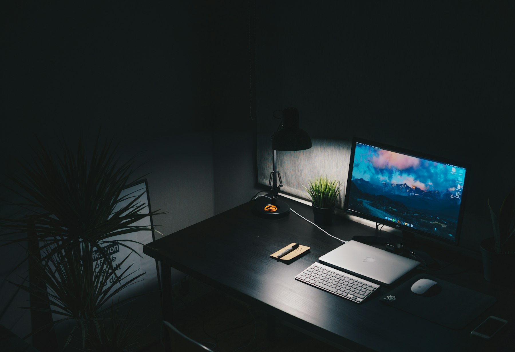 A desk at night with a monitor, keyboard and a single lamp