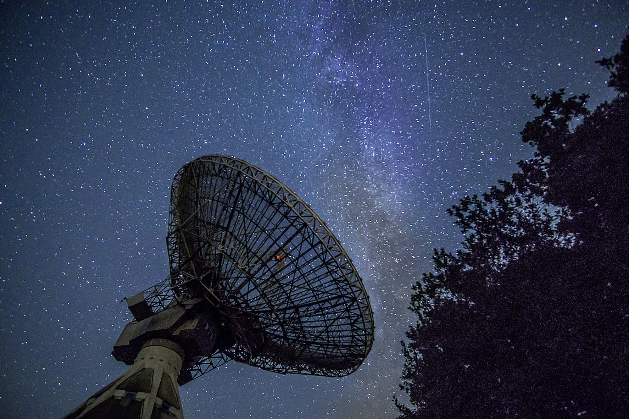 A radio telescope dish silhouetted against the Milky Way