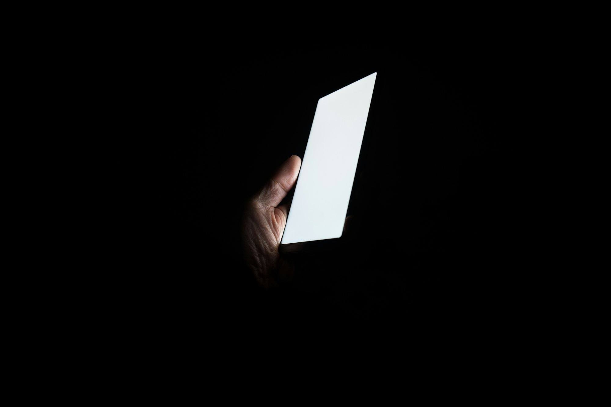 A hand holding a glowing phone screen in complete darkness
